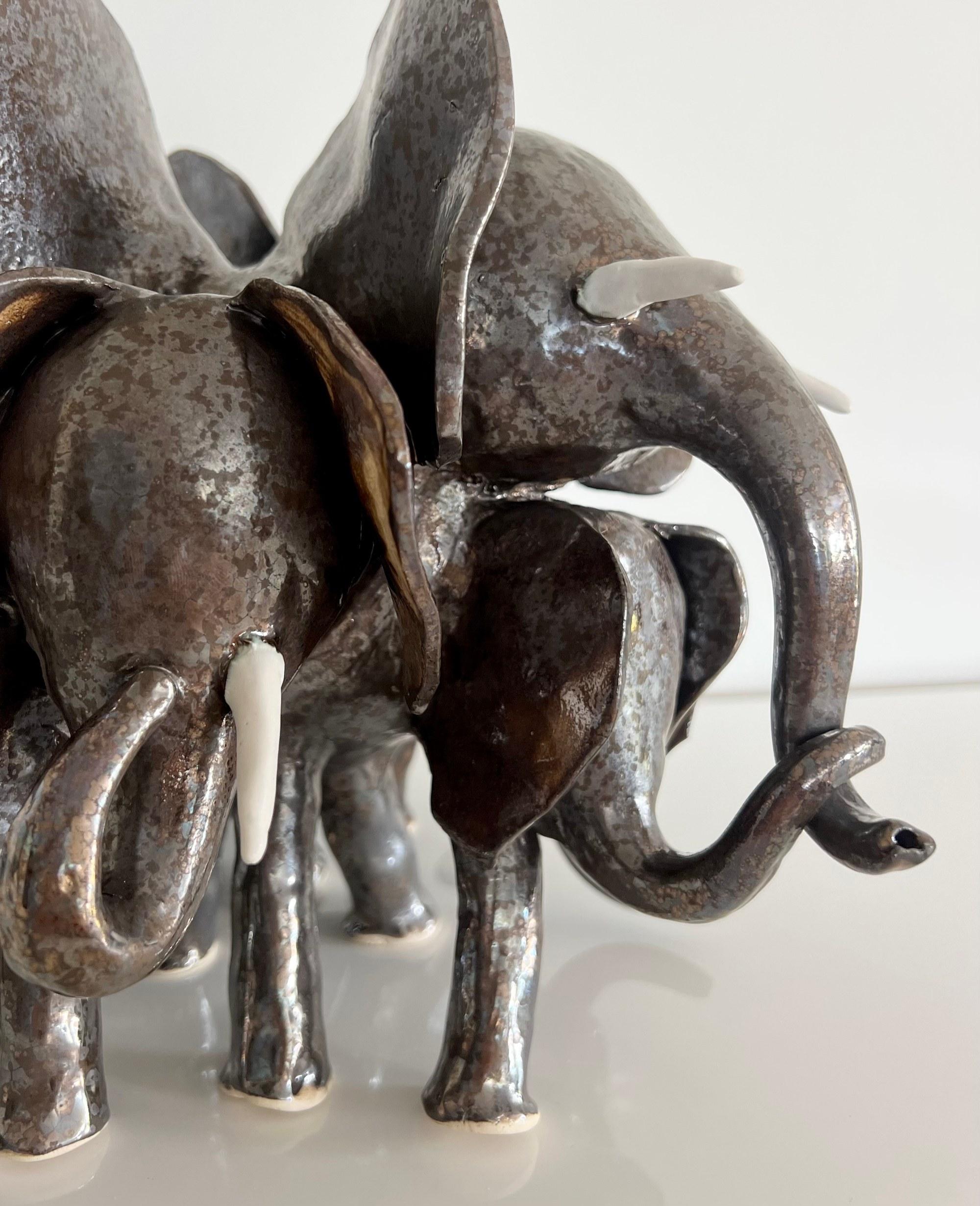 Close detail of a bronze lustre elephant herd: overlapping ears, curled trunks and white porcelain tusks