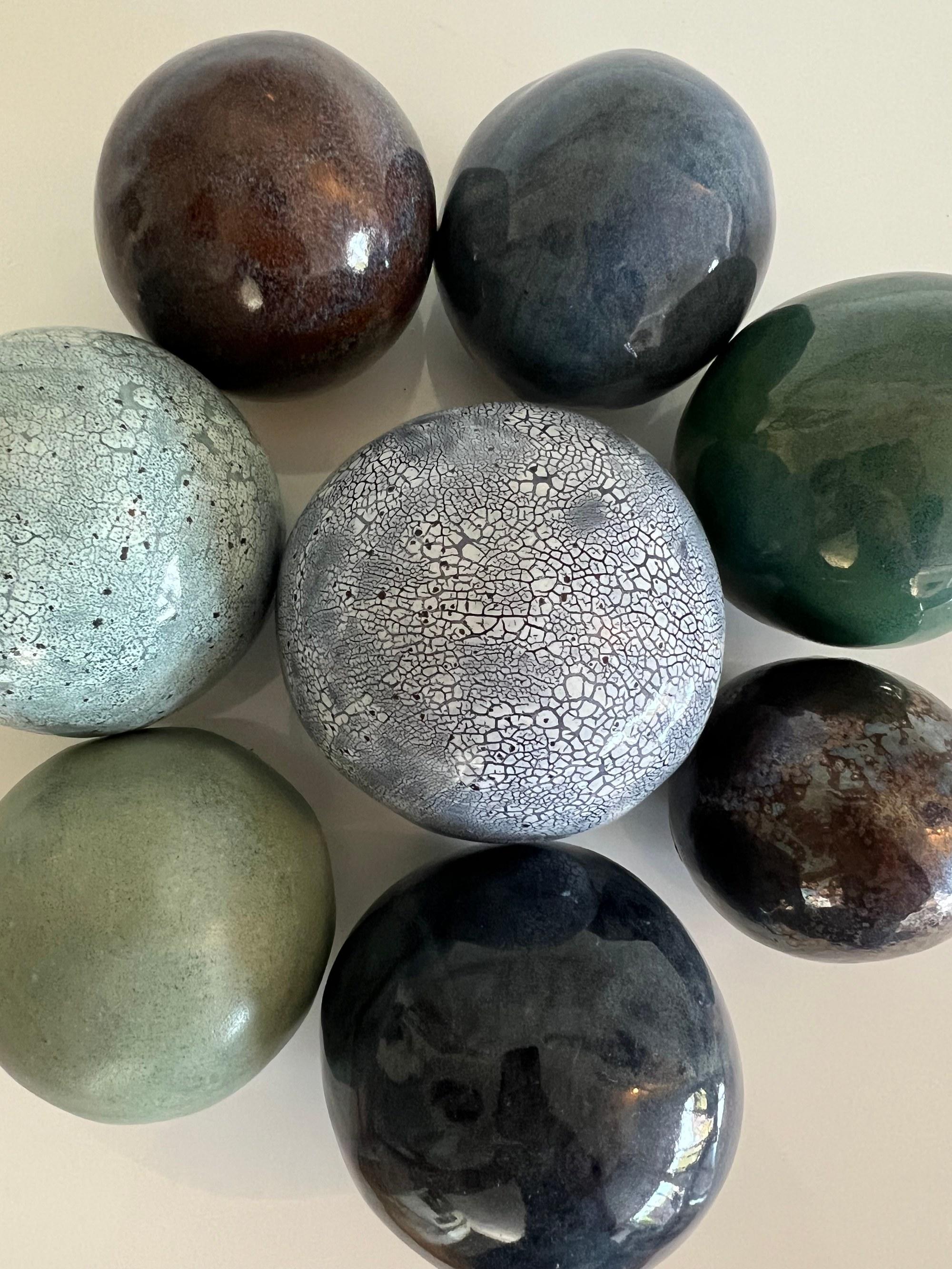 Eight glaze test pebbles laid out together — crackled white, moss green, bronze and near-black