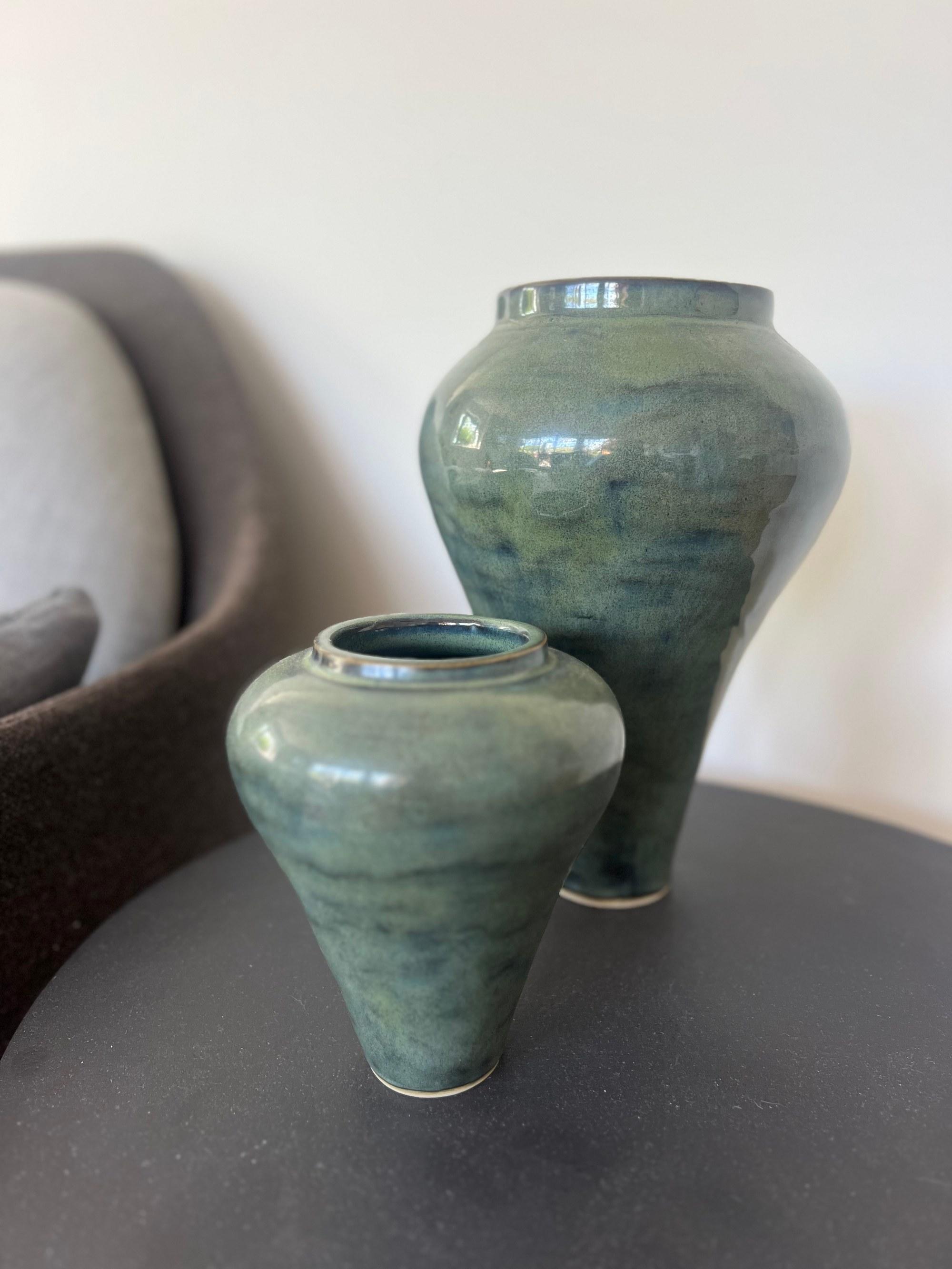 Two green glazed vases, one tall and one squat, on a dark side table