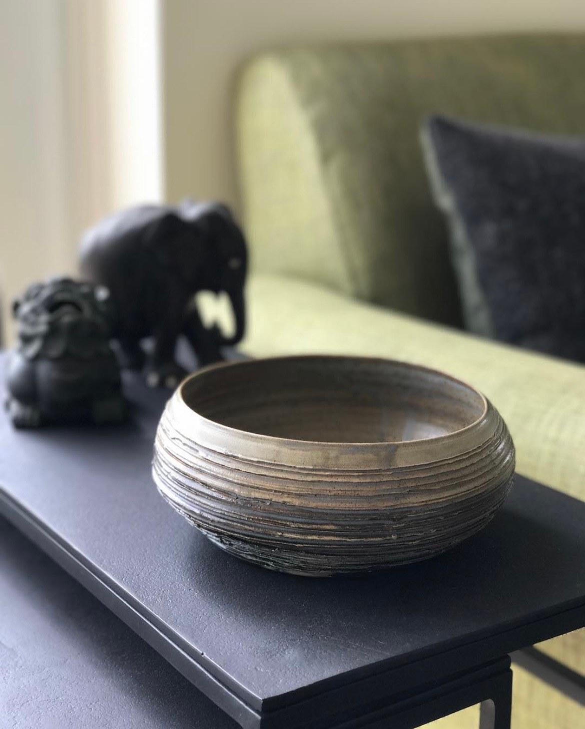 A ridged stoneware bowl on a black table, with carved wooden elephants behind it