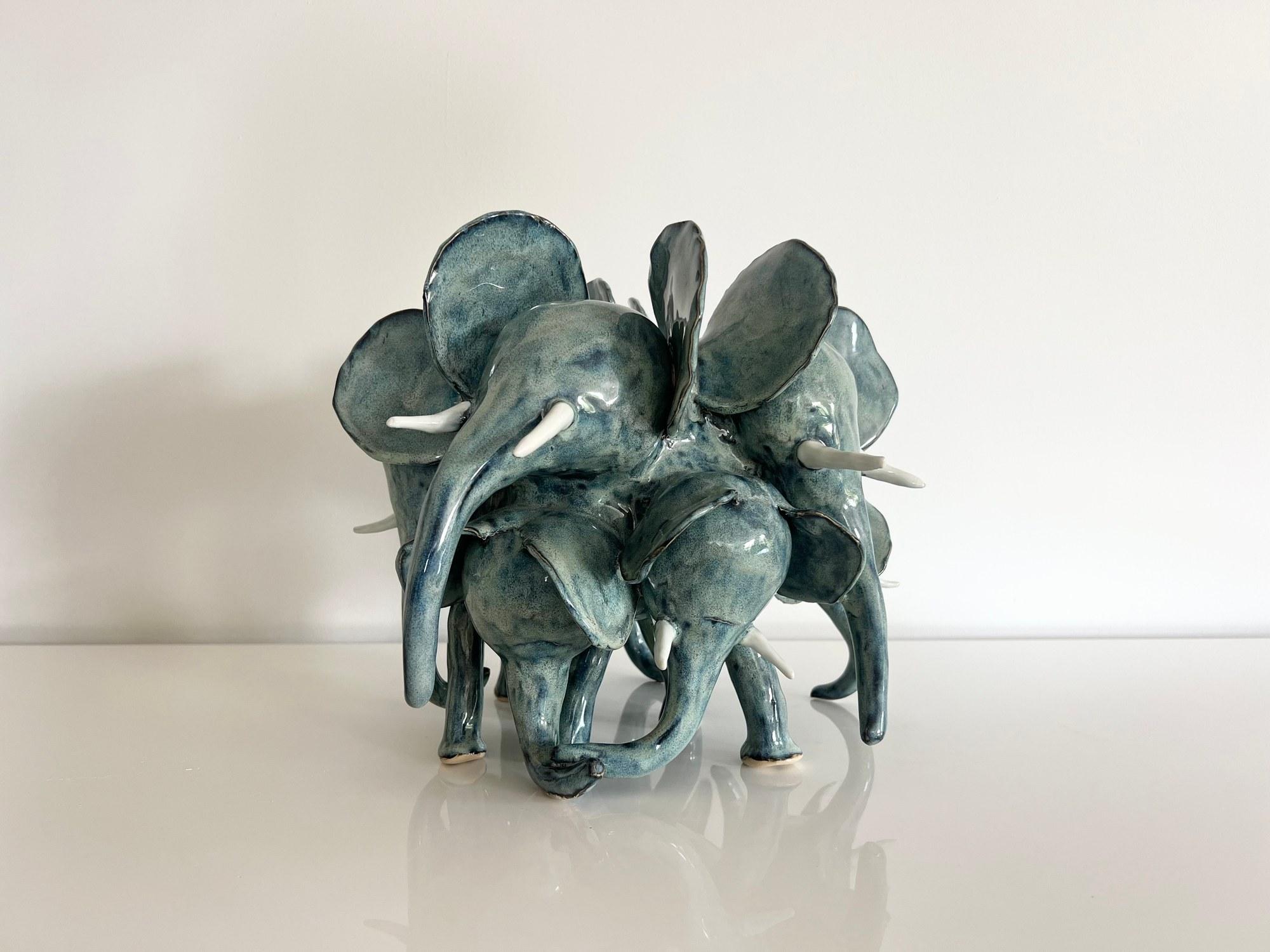 Handbuilt ceramic sculpture of six elephants standing back to back, glazed in mottled sea green with white porcelain tusks